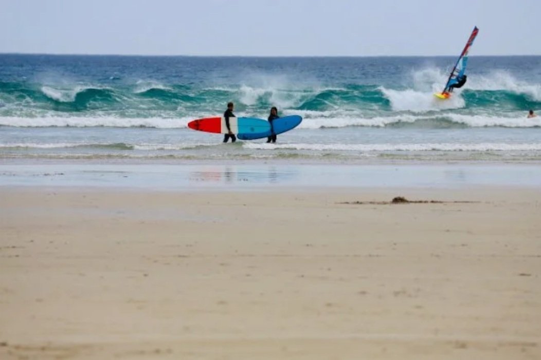 Surfers and a kitesurfer on the beach at Sandy Point