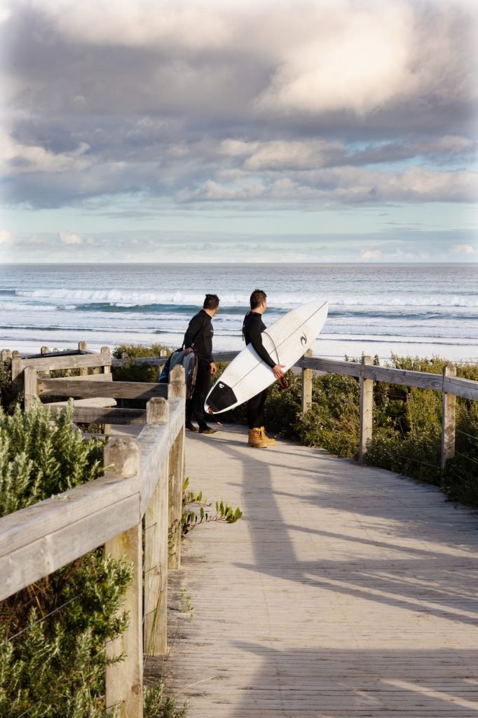 A surfer carrying a board along the beach track at Sandy Point